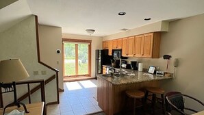 A spacious kitchen with wooden cabinets, a central island with stools, and a dining area with a table and chairs. - Lola’s Lodge Ski-In/Ski-Out 3 bedroom Lodge near hiking/golf (Lutsen)