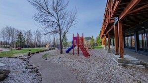 A playground with a slide and climbing structure, surrounded by a gravel path and trees. - Lola’s Lodge Ski-In/Ski-Out 3 bedroom Lodge near hiking/golf (Lutsen)