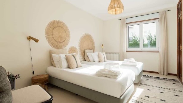 Een slaapkamer met een bed, nachtkastjes, een hanglamp en een raam met gordijnen.