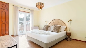 Een slaapkamer met een bed, een stoel, een houten nachtkastje en een groot raam.