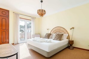 Een slaapkamer met een bed, een stoel, een houten nachtkastje en een groot raam.