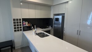 Une cuisine moderne avec des meubles blancs, un réfrigérateur en acier inoxydable et un four encastré.