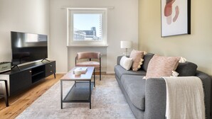 A modern living room with a flat-screen TV, a leather chair, a grey sofa, and a large window offering a city view. - Bright Matthäus 3 Room w/ Storage, near Kleinbasel, by Blueground (Basel)