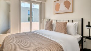 A bedroom with a bed, a nightstand, a lamp, and a window with a view of buildings. - Bright Matthäus 3 Room w/ Storage, near Kleinbasel, by Blueground (Basel)