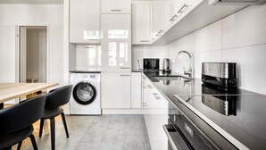 A modern kitchen with white cabinets, a built-in washing machine, a stainless steel range hood, and a black induction cooktop. - Upscale Gundelingen 4 Room w/ W/D & Storage, nr Train Station, by Blueground (Basel)