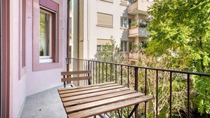 A balcony with a wooden bench, a metal railing, and a view of adjacent buildings and greenery. - Upscale Gundelingen 4 Room w/ W/D & Storage, nr Train Station, by Blueground (Basel)