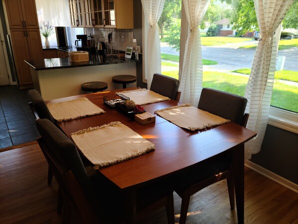 A dining area with a wooden table, four chairs, and a kitchen in the background.