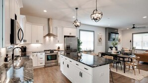 Une cuisine moderne avec des meubles blancs, un îlot central, des appareils en acier inoxydable et des luminaires suspendus.