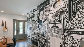 Une pièce avec une grande fresque murale en noir et blanc, une guitare et un coin repas comprenant une table et des chaises.