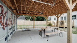 Ein überdachter Außenbereich mit Holzdecken und Betonböden, ausgestattet mit Picknicktischen und einem Grill.