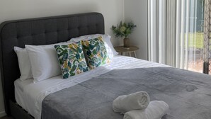 Een slaapkamer met een donker hoofdbord, wit beddengoed, een grijze deken en twee opgerolde handdoeken op het bed.