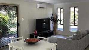Een moderne woonkamer met een eettafel, een grijze bank, een televisie en een groot raam.