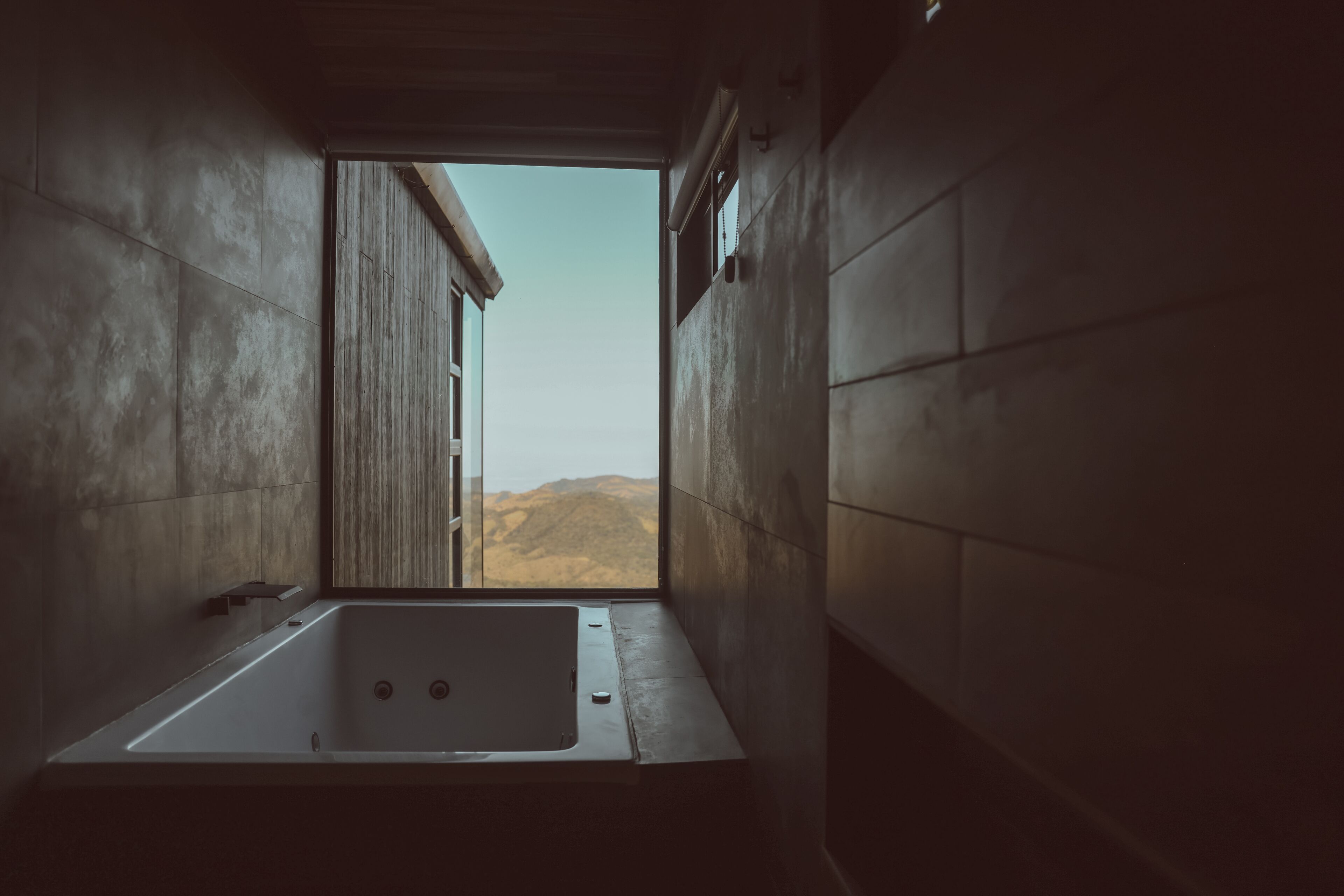 Un baño moderno con una bañera grande, una puerta de madera y vistas a montañas.