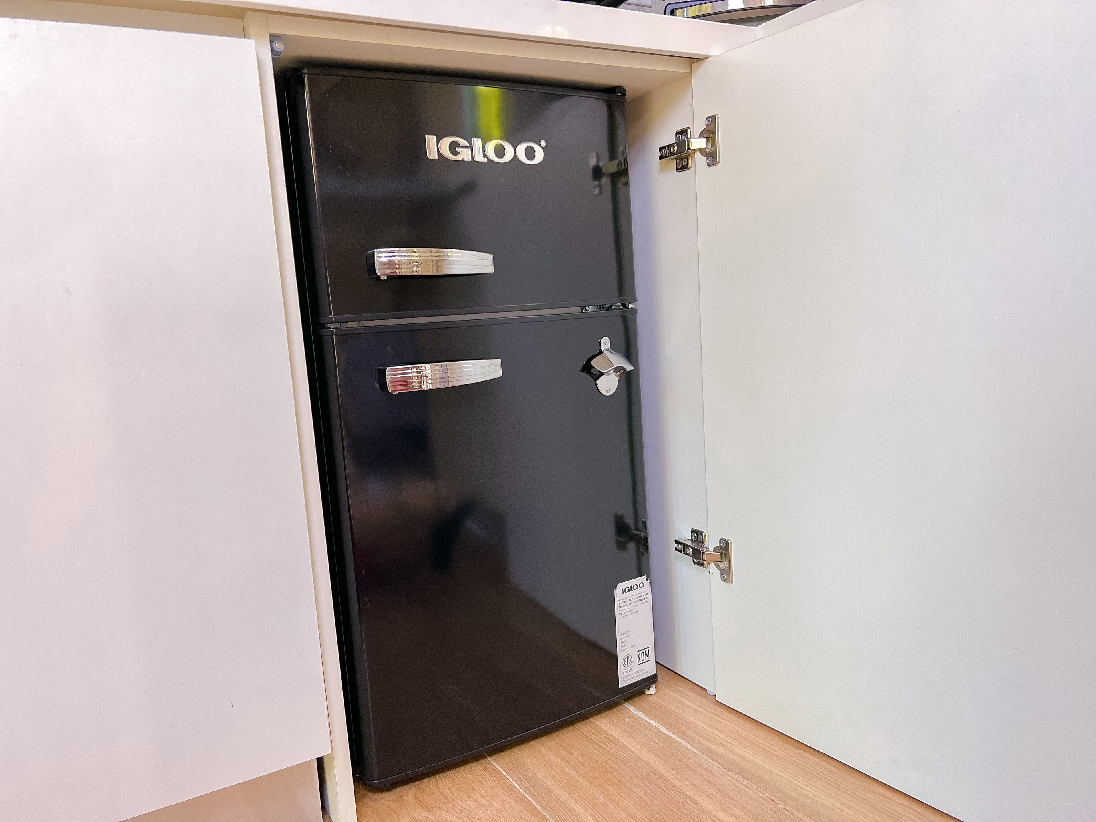 A black metal safe with the brand IGLOO, located in a room with white walls and a wooden floor.