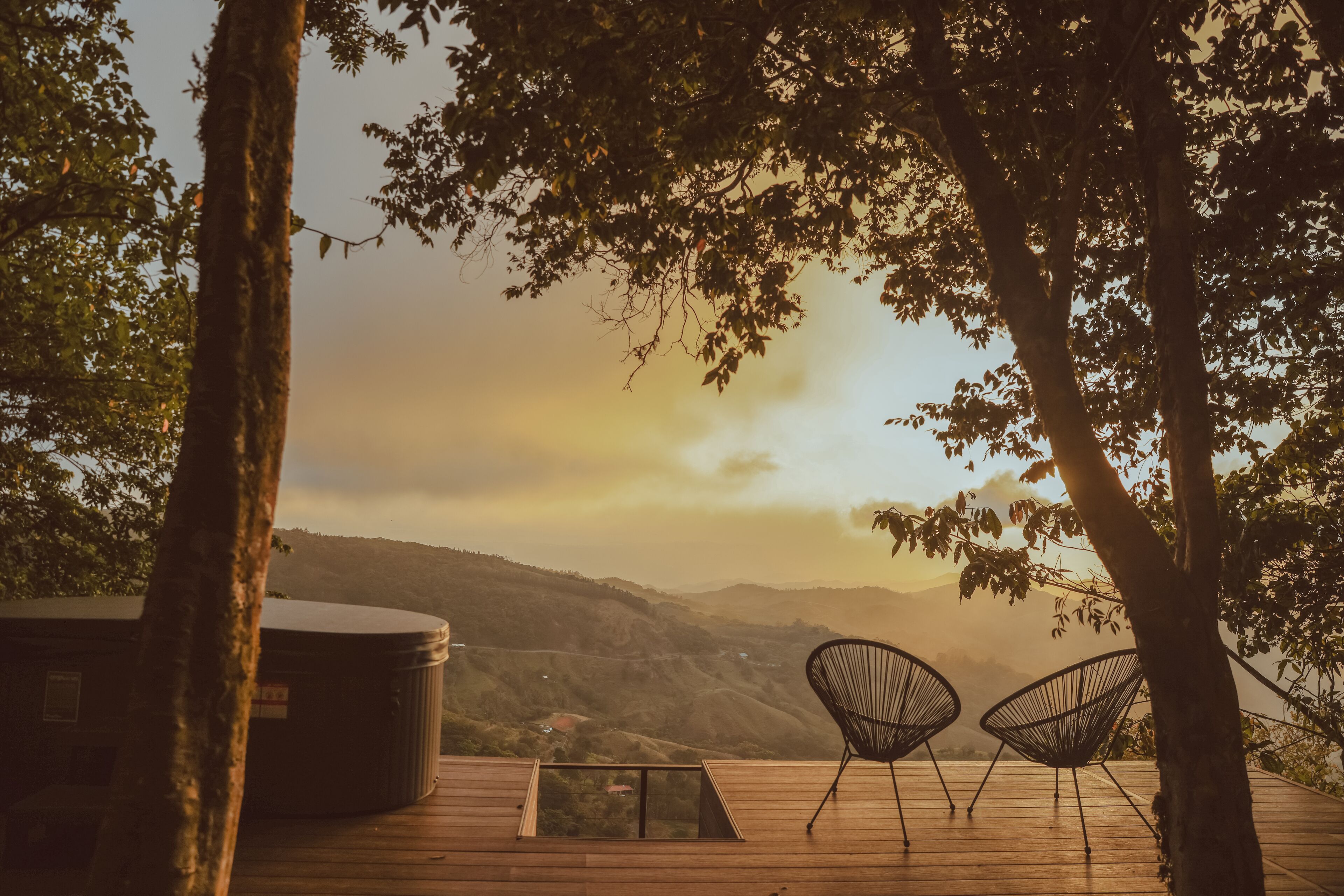 A wooden deck with two black wire chairs and a hot tub, overlooking a mountainous landscape.