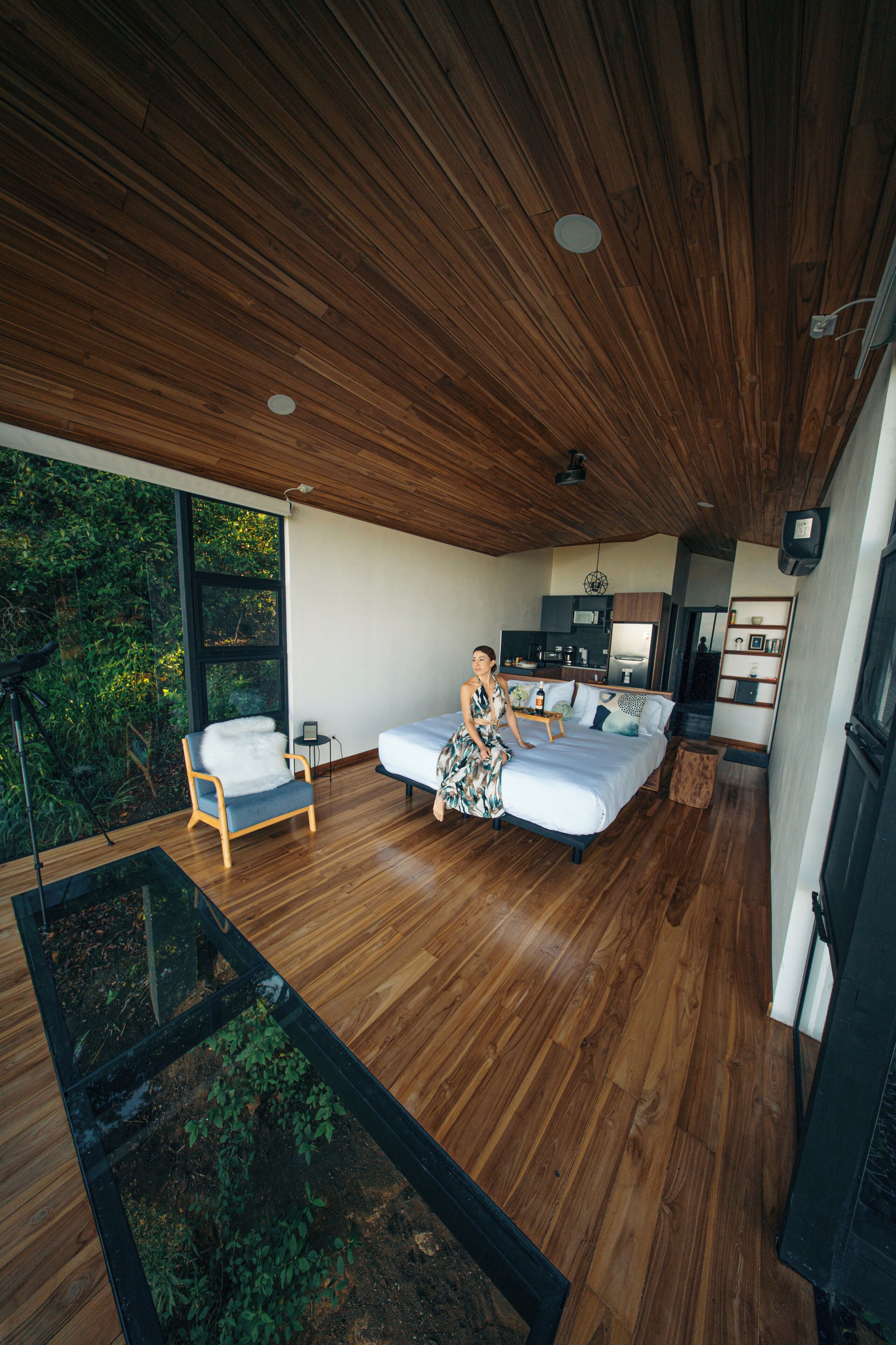Quarto moderno com uma cama grande, teto de madeira e vista para o verde lá fora.