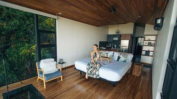 Quarto moderno com uma cama grande, teto de madeira e vista para o verde lá fora.