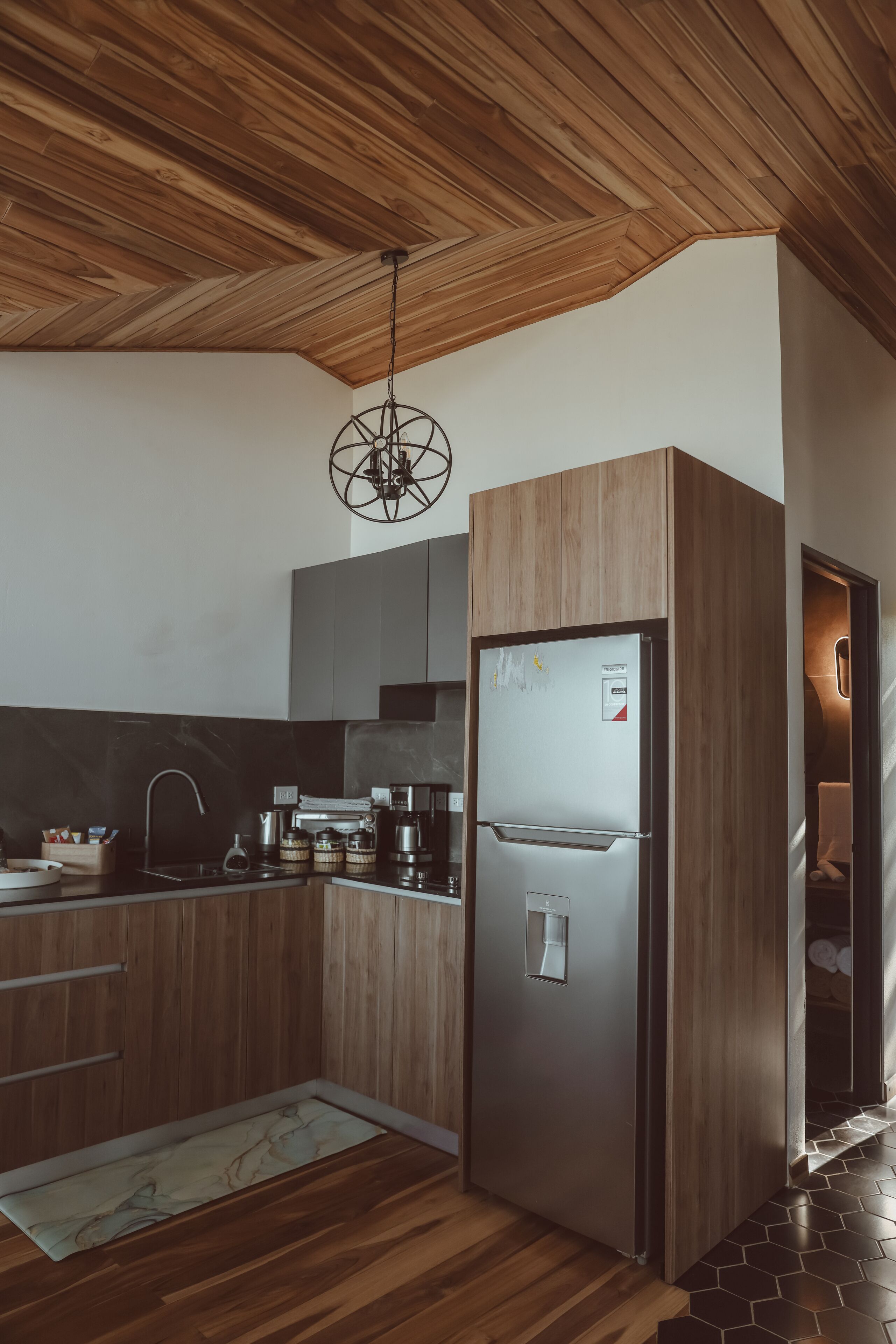 A modern kitchen with wooden cabinetry, a stainless steel refrigerator, and a hanging light fixture.