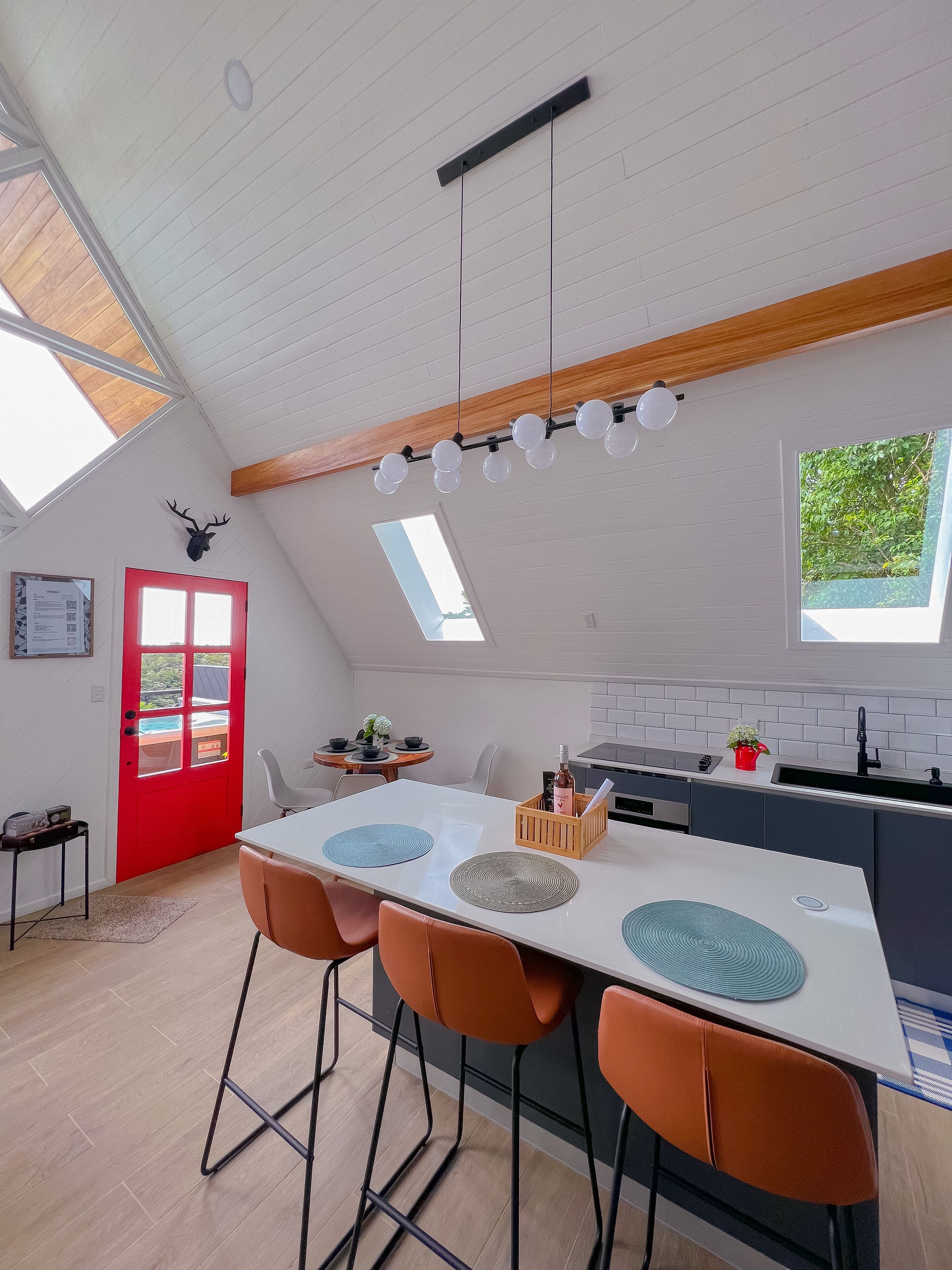 Une cuisine moderne avec un plan de travail blanc, une porte rouge et une lucarne.