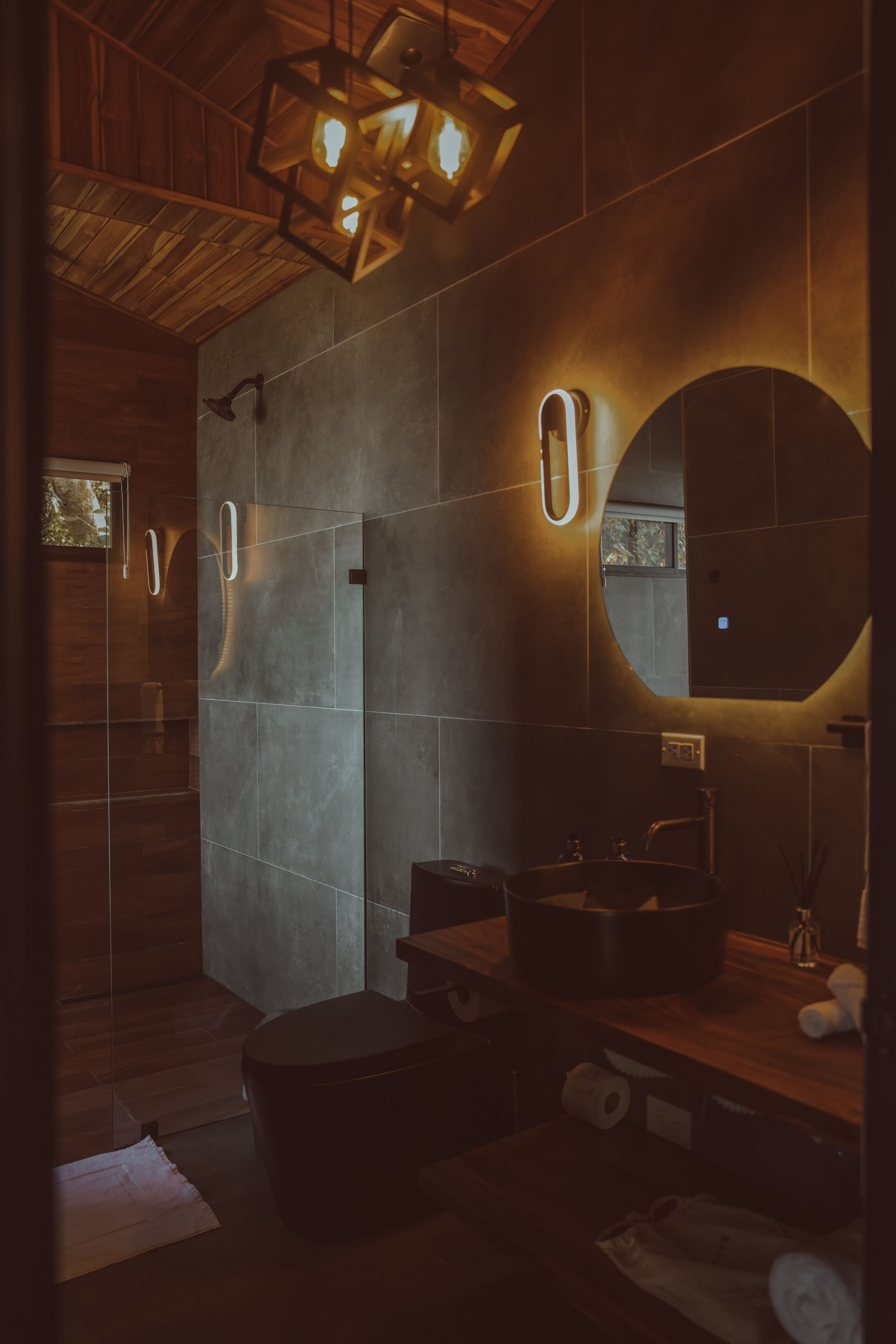 Un bagno moderno con soffitto in legno, una vasca freestanding, uno specchio rotondo e un lavabo incassato.