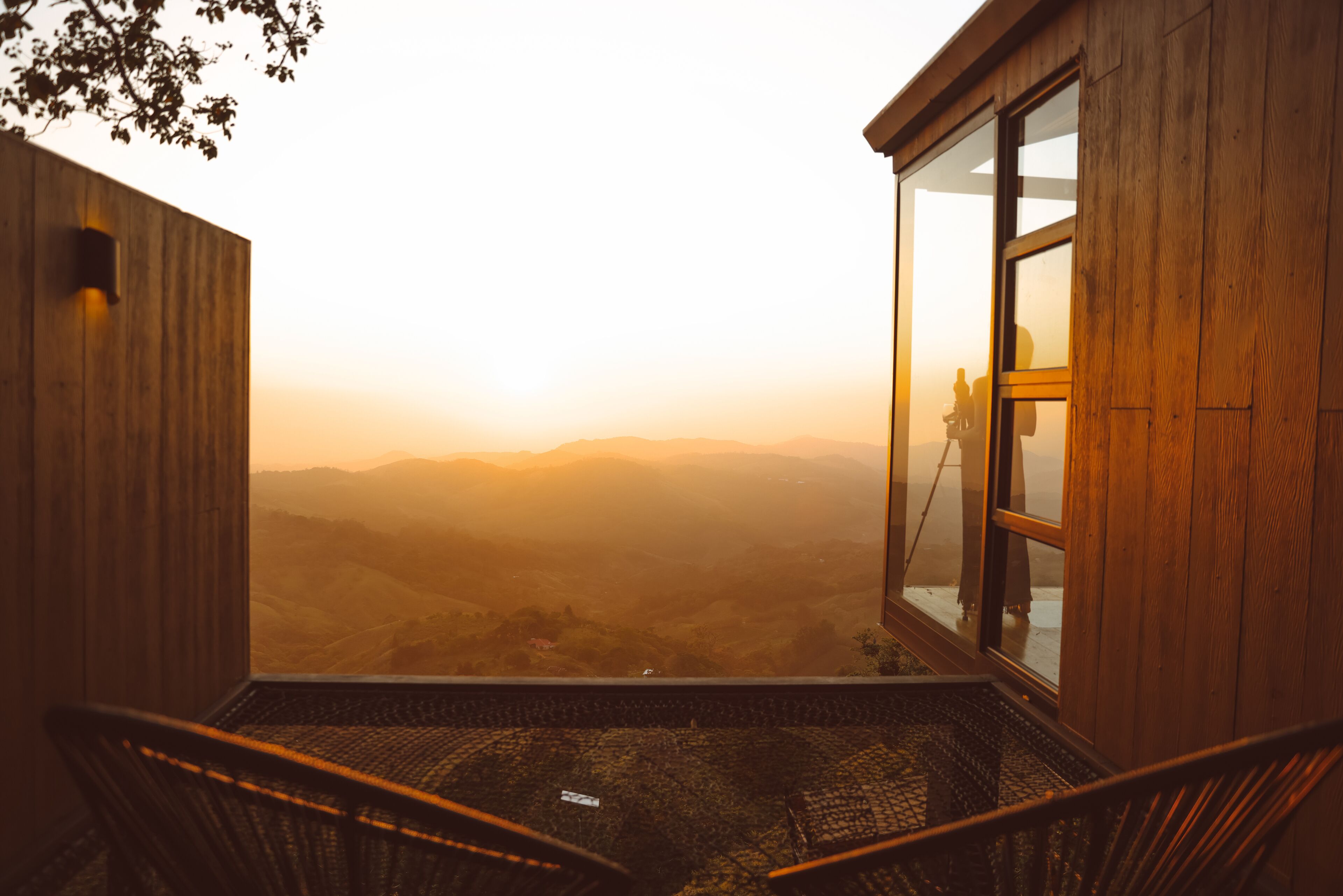 Una cabaña de madera con un balcón de cristal con vistas a un valle.