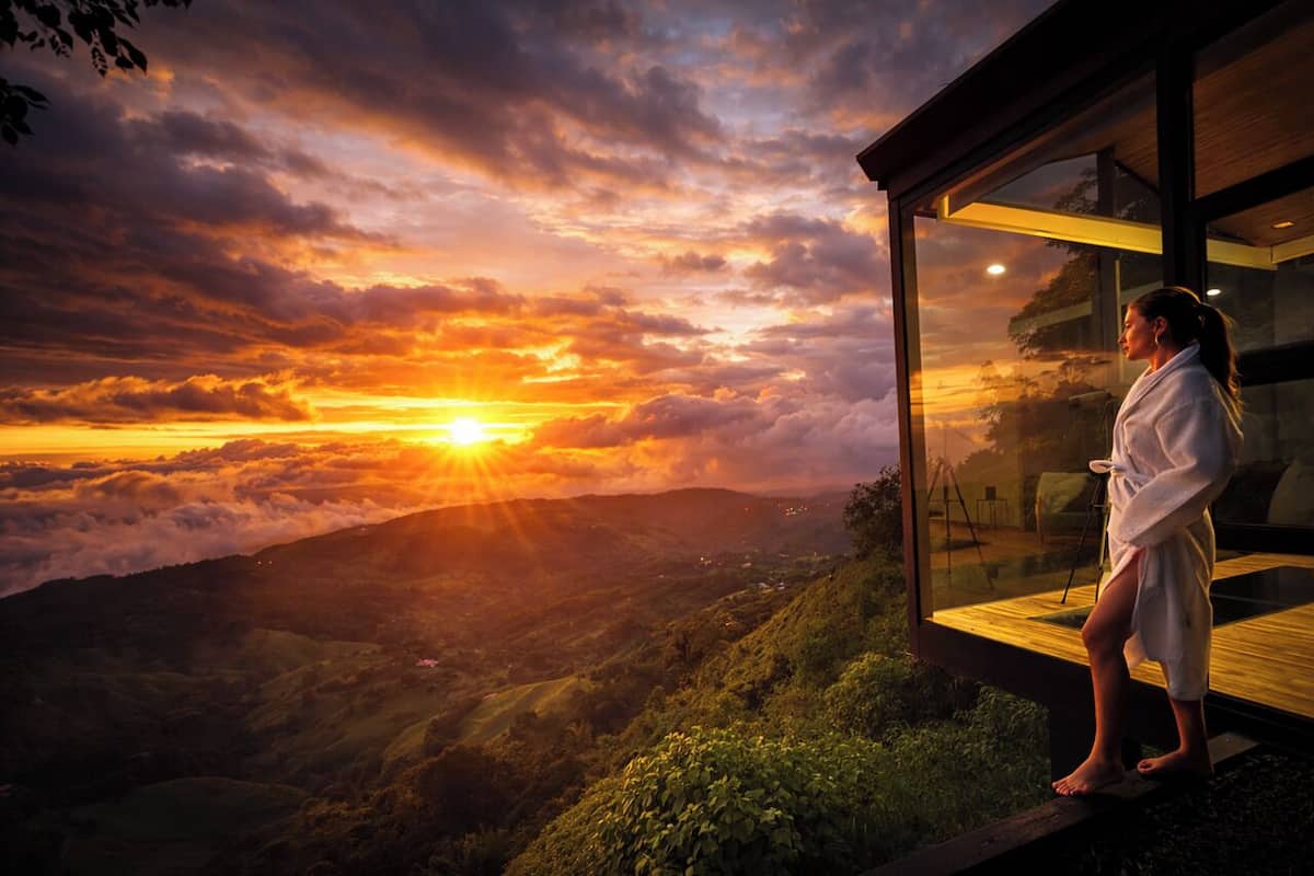 A person standing by a glass wall overlooking a sunset view.