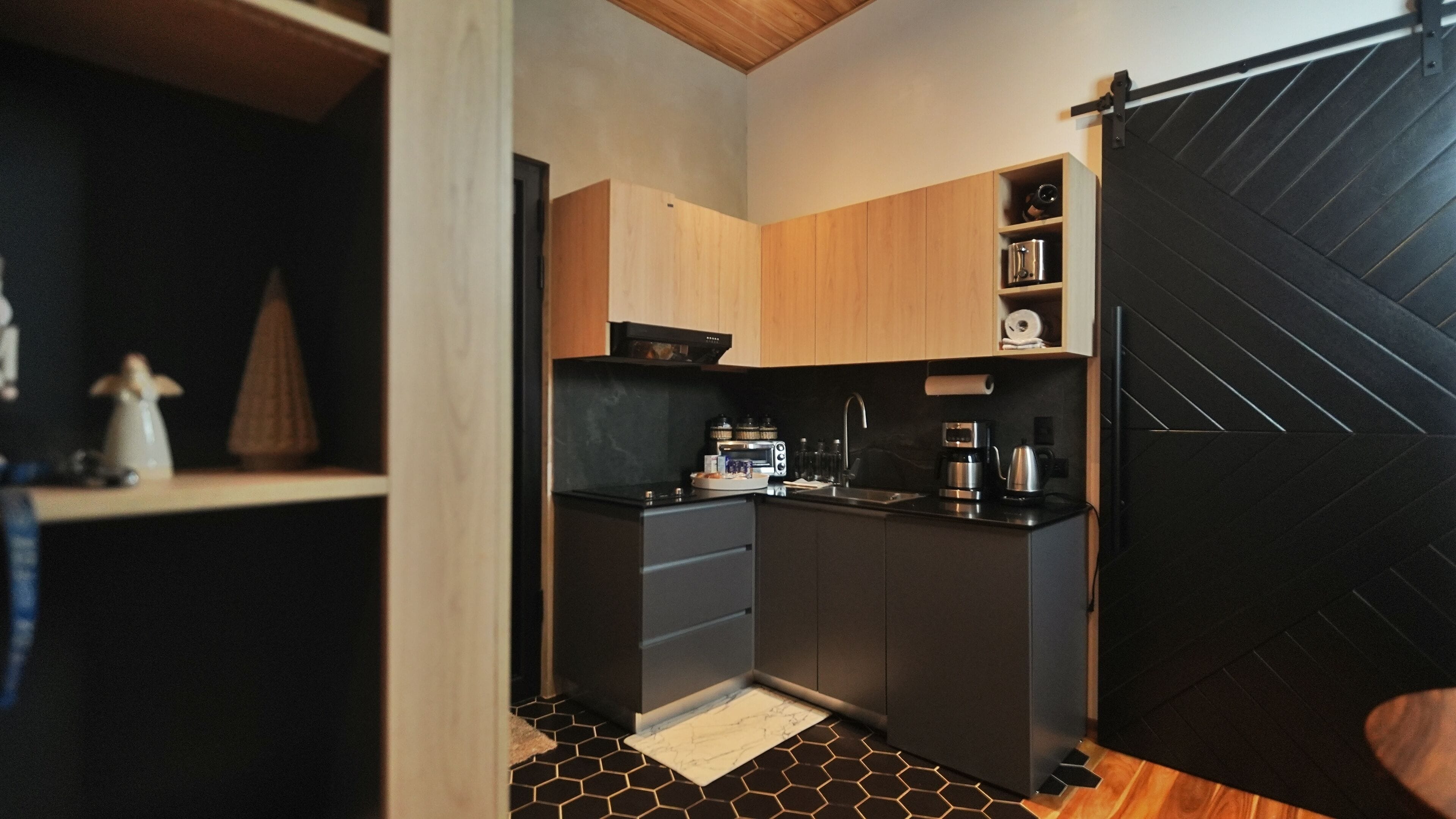 A compact kitchen with wooden cabinets, a black countertop, and a black and white tiled floor.