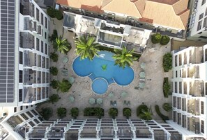 Luchtbeeld van een hotel met een centraal gelegen zwembad, omringd door palmbomen en ligbedden.