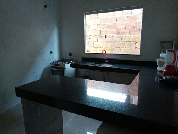 A kitchen with a black countertop, a gas stove, a sink, and a window with a brick wall view.