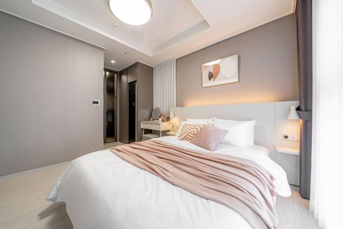 A modern hotel room with a large bed, bedside table, and a mirror.