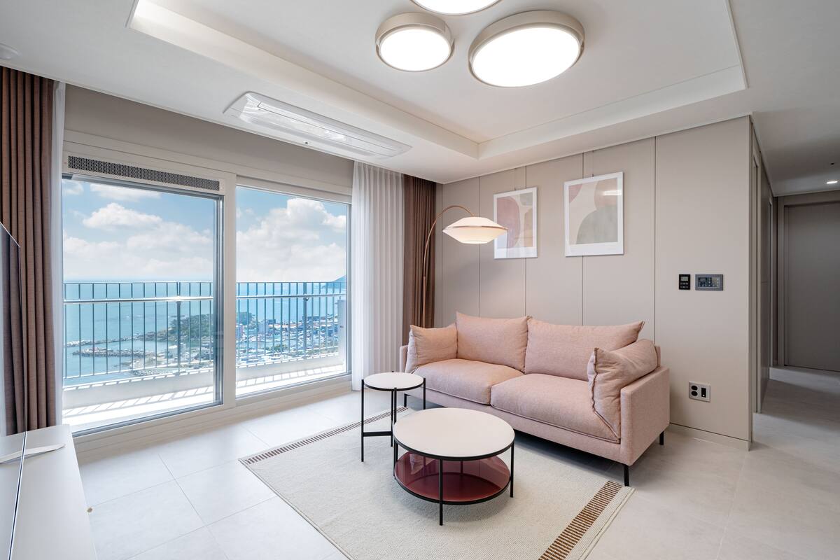 Una sala de estar moderna con un ventanal grande, un sofá, una mesita de centro y vistas de la ciudad.