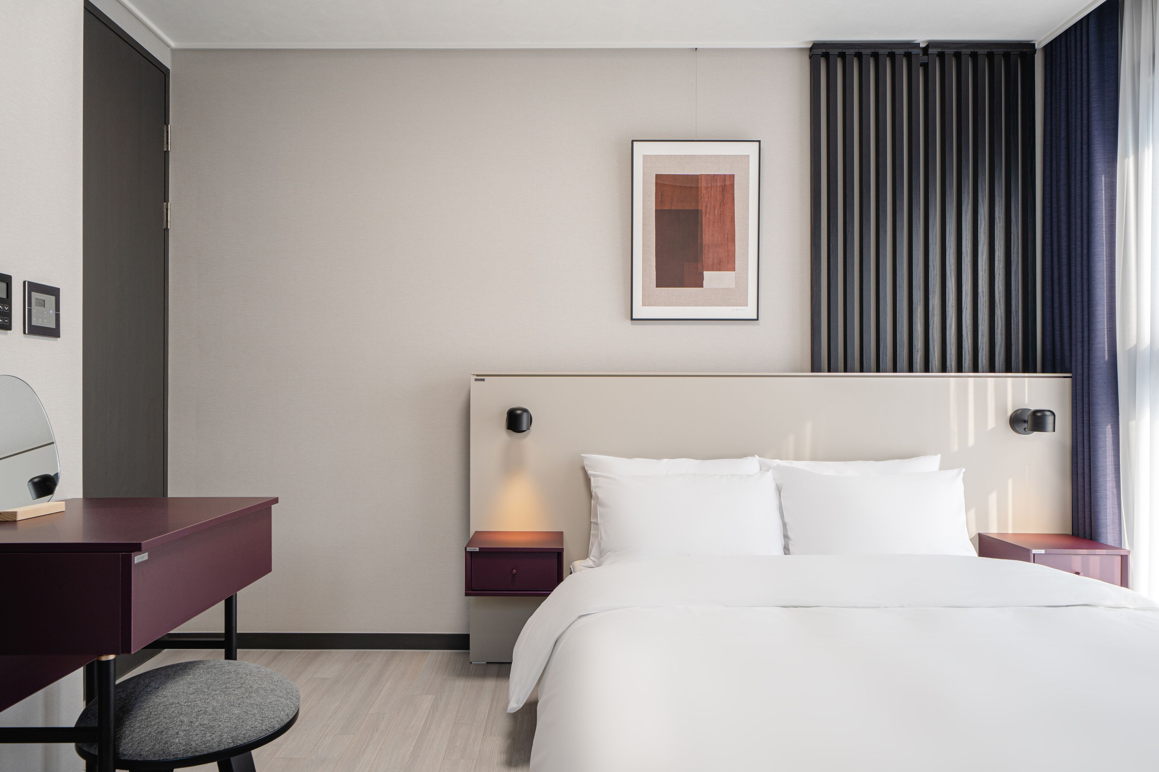 Una camera d'hotel con un letto, una scrivania, una sedia, un comodino e una lampada fissata al muro.
