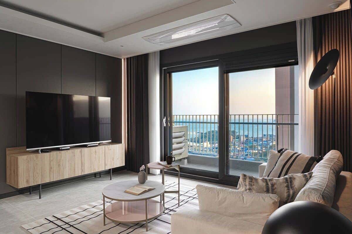 Una sala de estar moderna con un televisor grande, un sofá, una mesa de centro y un balcón con vistas a la ciudad.
