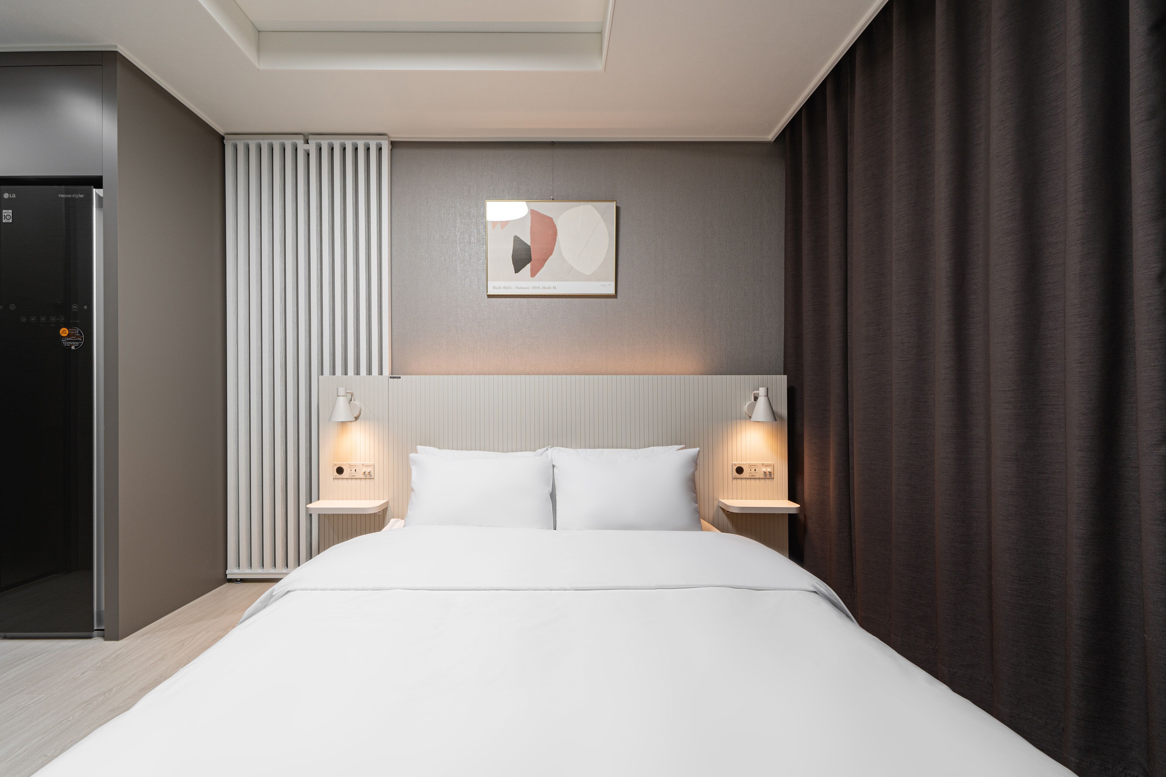 Una habitación de hotel moderna con una cama grande, dos lámparas de noche, una obra de arte colgada en la pared y un radiador.