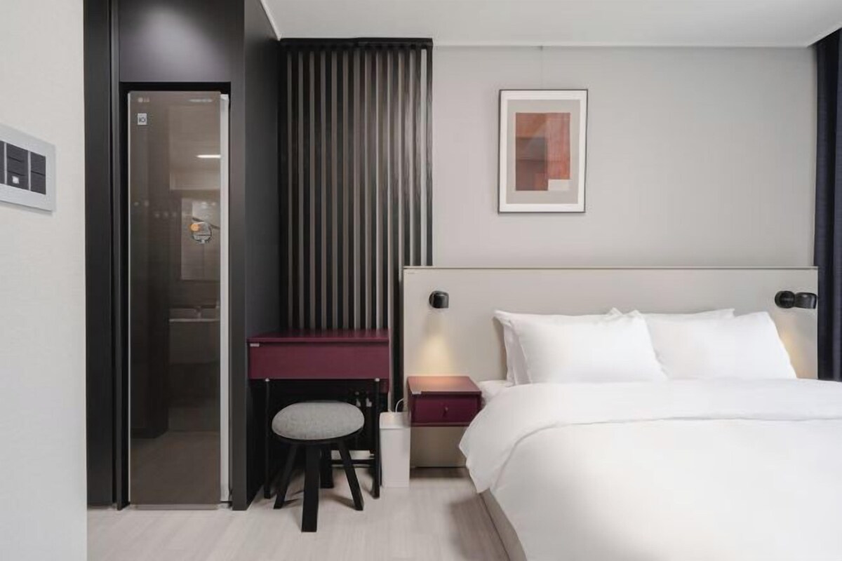A hotel room with a bed, a desk with a chair, a nightstand, and a framed picture on the wall.