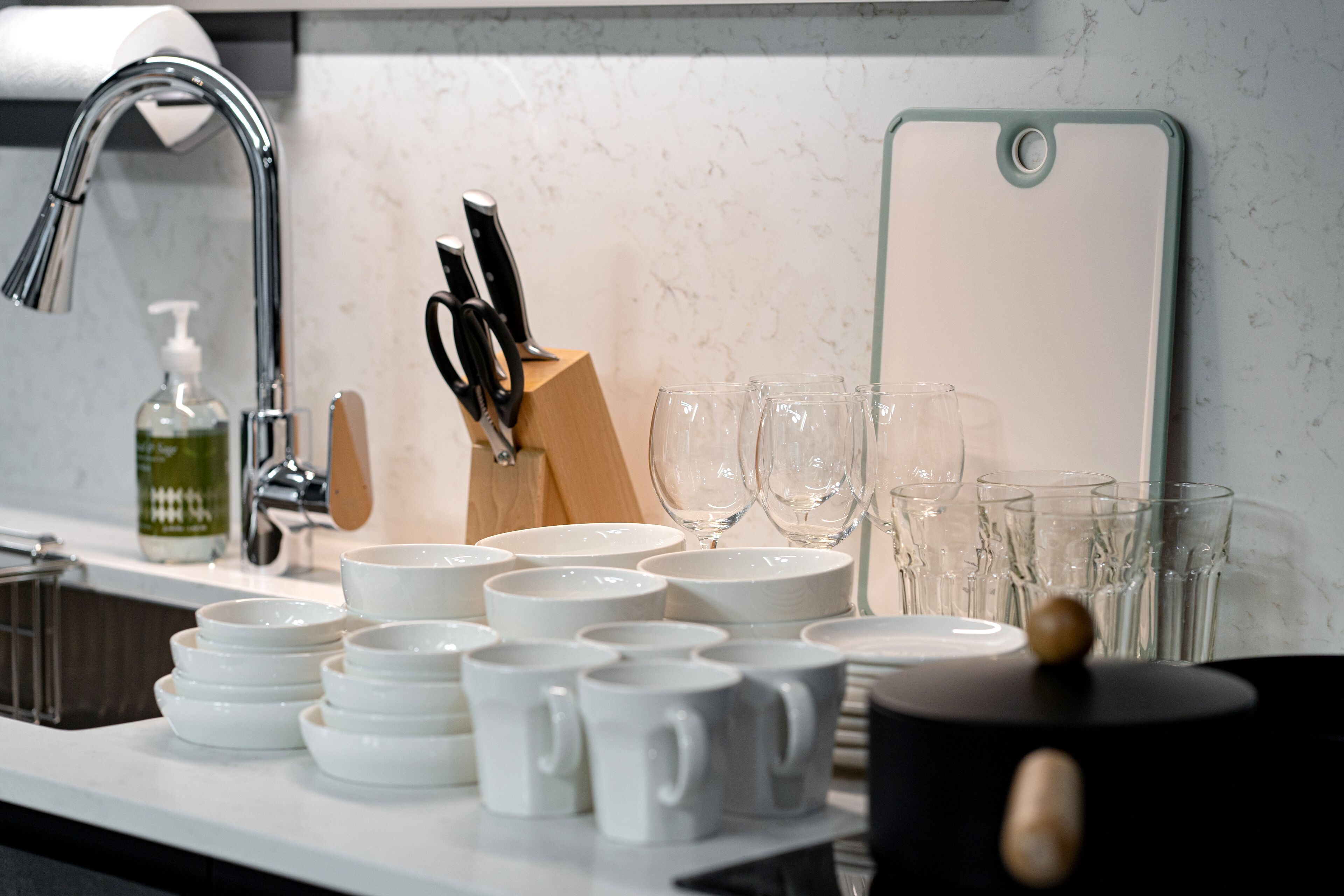 A kitchen counter with various white dishes, a knife block, and a glassware rack.