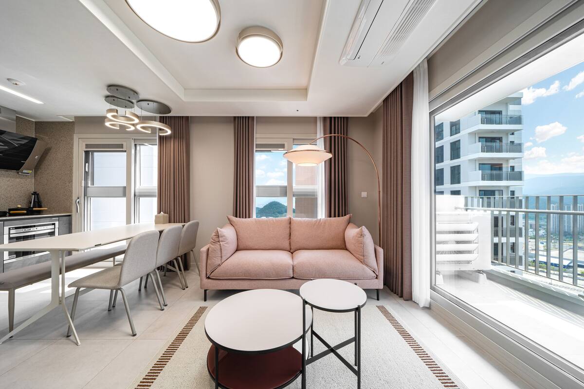 Una habitación de hotel moderna con sofá, mesa de comedor, sillas y vista a la ciudad.