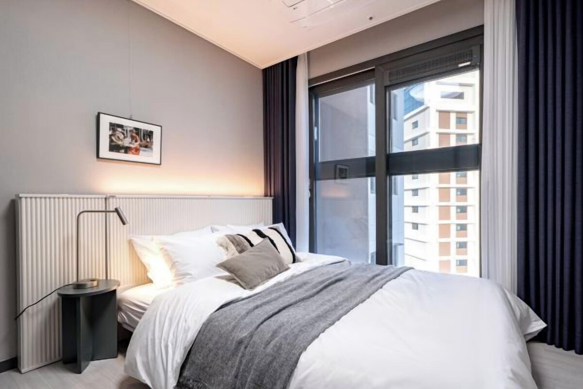 A modern hotel room with a large bed, a bedside table, a radiator, and a window with curtains.