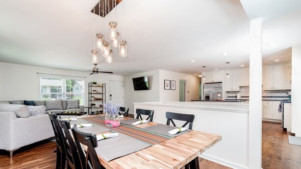 Una cocina moderna con armarios blancos, una isla central y una zona de comedor con mesa y sillas de madera.