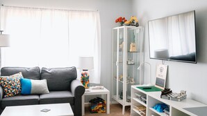 A living room with a grey sofa, white coffee table, and a TV mounted on the wall. - Builditplace! Kid friendly Stay, Play and Create! (Akron)