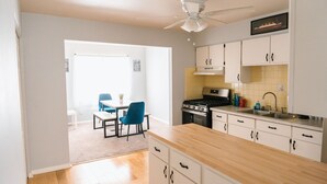 A kitchen with white cabinets, a wooden countertop, and a ceiling fan. There is a dining area with a table and chairs visible through an open doorway. - Builditplace! Kid friendly Stay, Play and Create! (Akron)