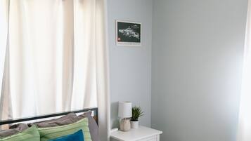 A neatly made bed with pillows, a bedside table with a lamp and a plant, and a framed picture on the wall.