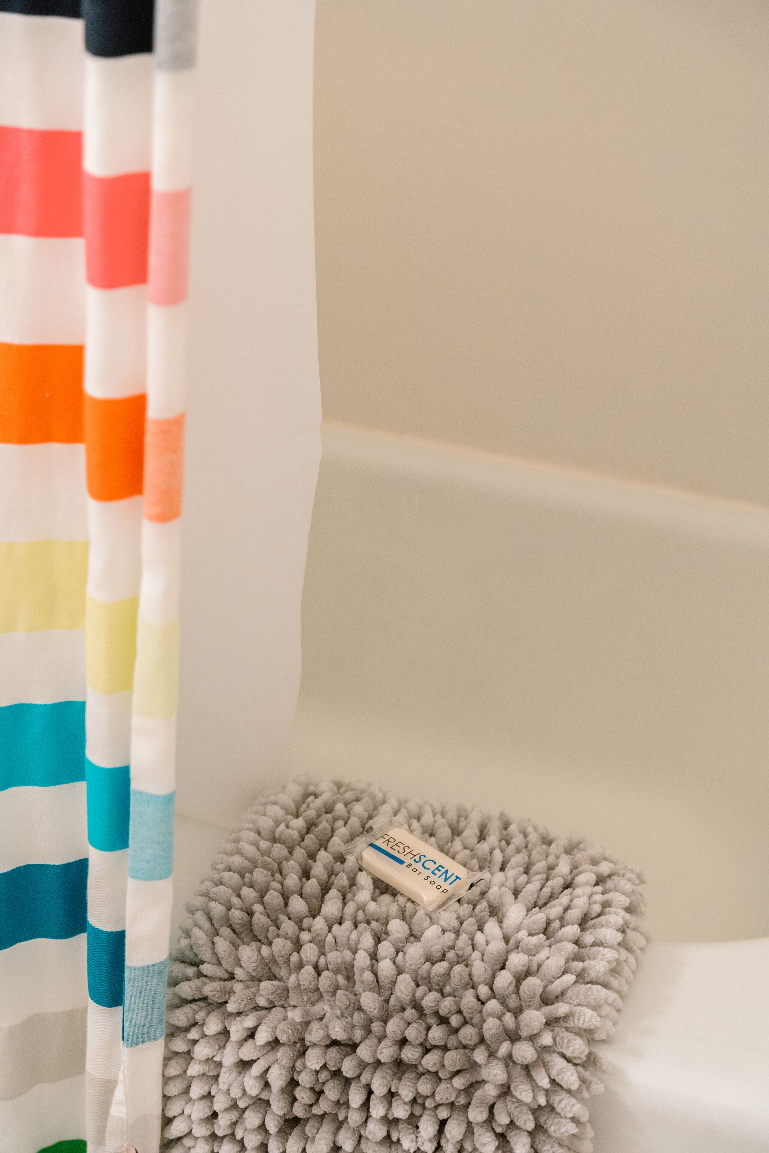 A bathroom with a striped shower curtain, a fluffy gray bath mat, and a bottle of air freshener.