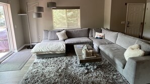 Un salon moderne avec un canapé d’angle gris, un tapis moelleux et une lampe sur pied.