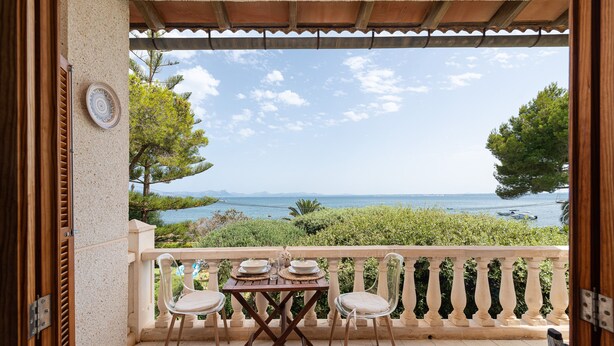 Un balcon avec une table et des chaises, offrant une vue panoramique sur la mer et la verdure.