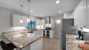 A modern kitchen with white cabinets, granite countertops, stainless steel appliances, and pendant lighting.