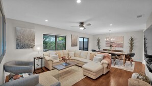 A spacious living room with a large sectional sofa, a coffee table, and a dining area with a chandelier.