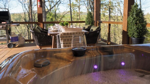 Et spabad med kontrolpanel, omgivet af fletstole og et bord med et glas vand.