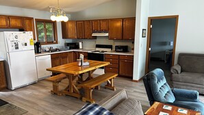 A modern kitchen with wooden cabinets, a dining table with benches, and a living area with a sofa and a coffee table. - Lakefront Cottage on South Manistique Lake (curtis)