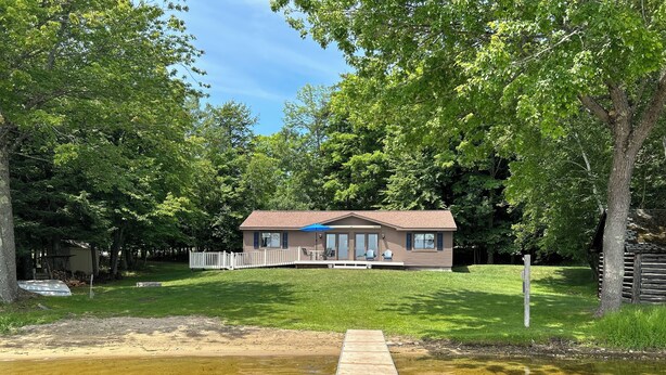 A cabin with a dock extending into a clear lake, surrounded by trees. - Lakefront Cottage on South Manistique Lake (curtis)